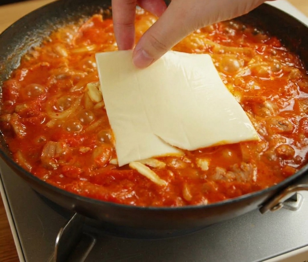 Dłoń kładąca kwadratowy plaster żółtego sera topionego na rozpuszczającej się mozzarelli i makaronie udon.