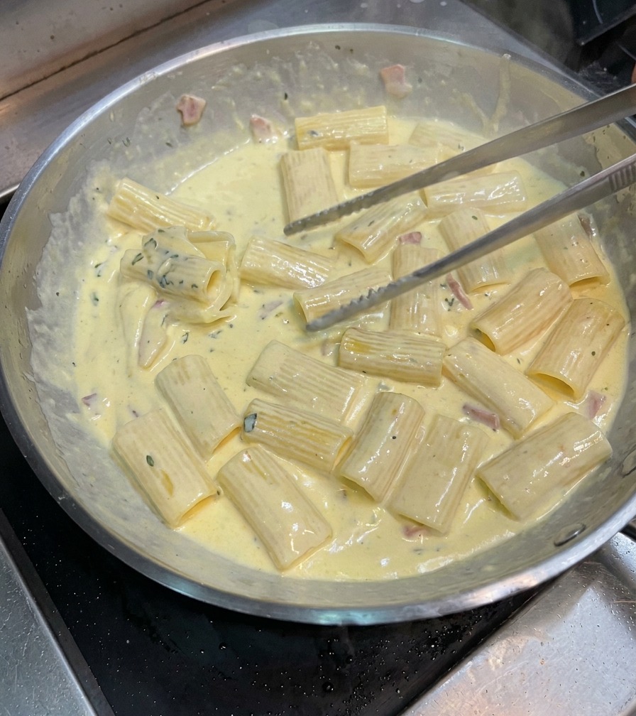 Mieszanie makaronu szczypcami na patelni w gęstym, kremowym sosie carbonara.