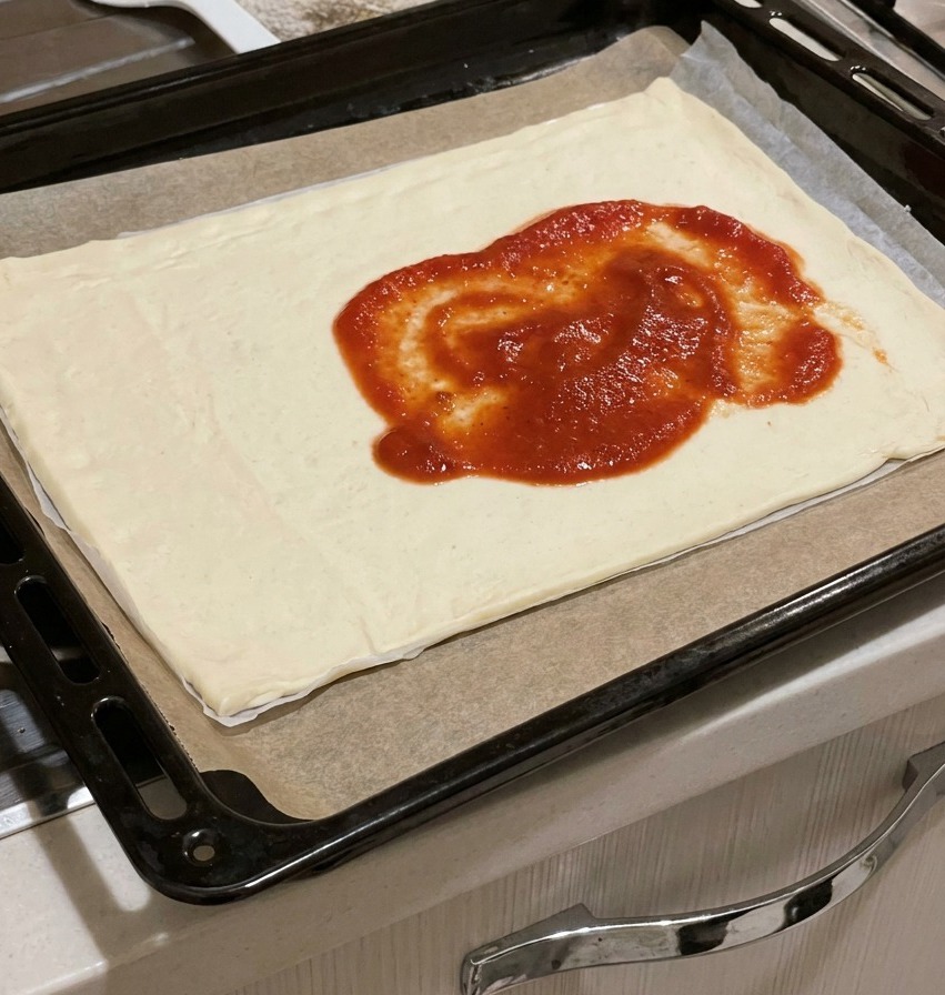 Gęsty czerwony sos pomidorowy nałożony na środek surowego prostokątnego ciasta do pizzy.