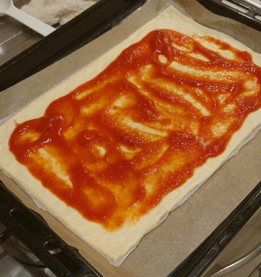Prostokątny spód do pizzy z czerwonym sosem pomidorowym rozprowadzonym równomiernie, z widocznym czystym brzegiem ciasta.