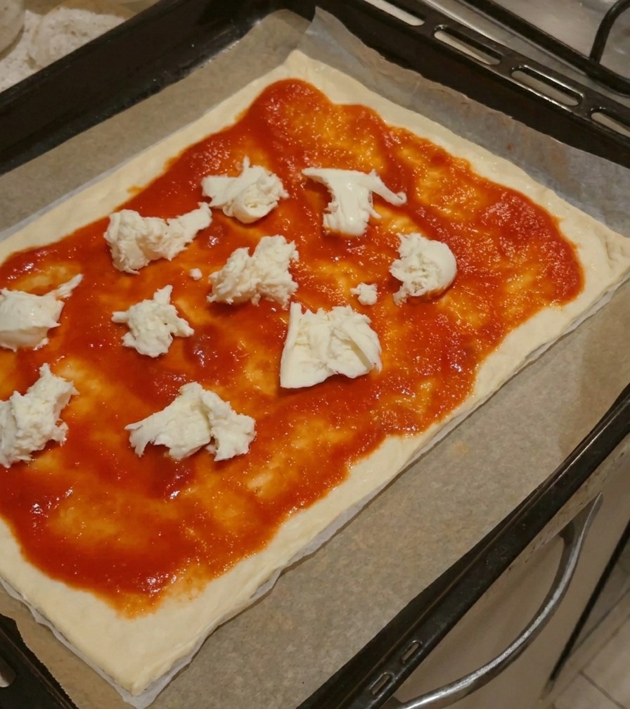 Duże kawałki świeżej białej mozzarelli ułożone na sosie pomidorowym na spodzie do pizzy.