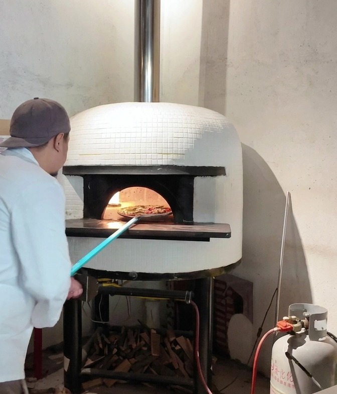 Pizza zsuwana z łopaty do wnętrza rozgrzanego pieca opalanego drewnem.