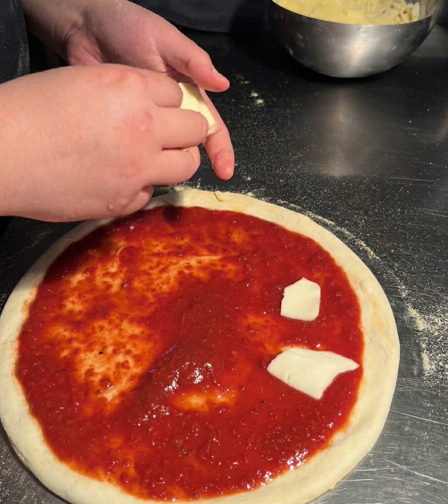 Osoba układająca ręcznie rwane kawałki białej mozzarelli na spodzie pizzy pokrytym sosem.