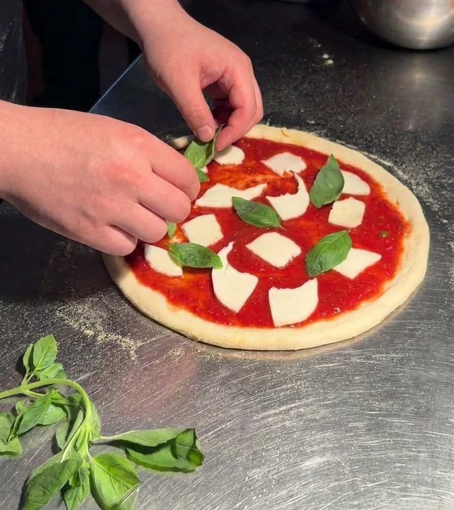 Dłonie układające świeże, jasnozielone liście bazylii na surowej pizzy Margherita.