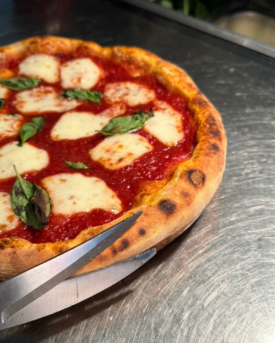 Zbliżenie na ostre nożyce kuchenne przecinające puszysty brzeg gorącej pizzy Margherita.