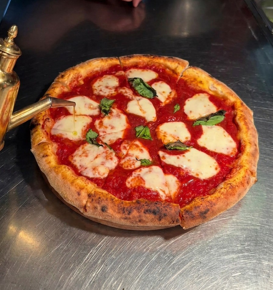 Oliwa z oliwek extra virgin lana ze złotego dozownika na pokrojoną pizzę Margherita.