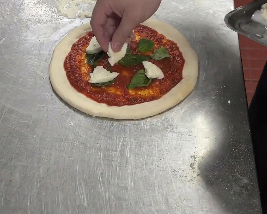 Porwane kawałki białej mozzarelli di bufala dodawane na pizzę z sosem pomidorowym i bazylią.