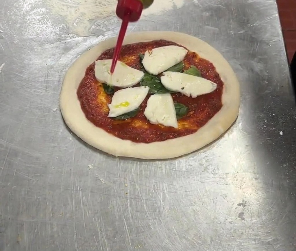 Czerwona butelka dozująca oliwę extra virgin na pizzę z sosem, bazylią i mozzarellą.