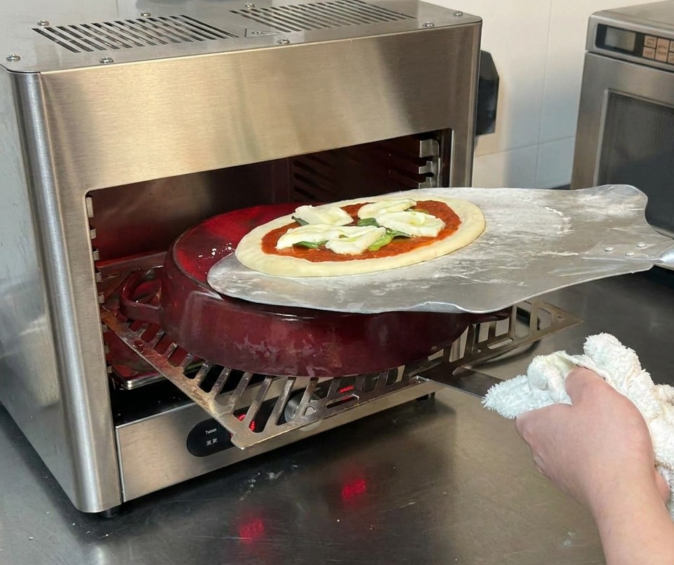 Metalowa łopata do pizzy zsuwająca surową pizzę na czerwony garnek żeliwny wewnątrz pieca.