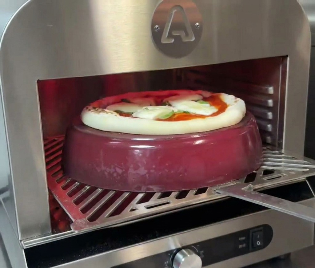 Pizza piekąca się na czerwonym garnku żeliwnym; widać, jak brzegi zaczynają rosnąć i brązowieć.