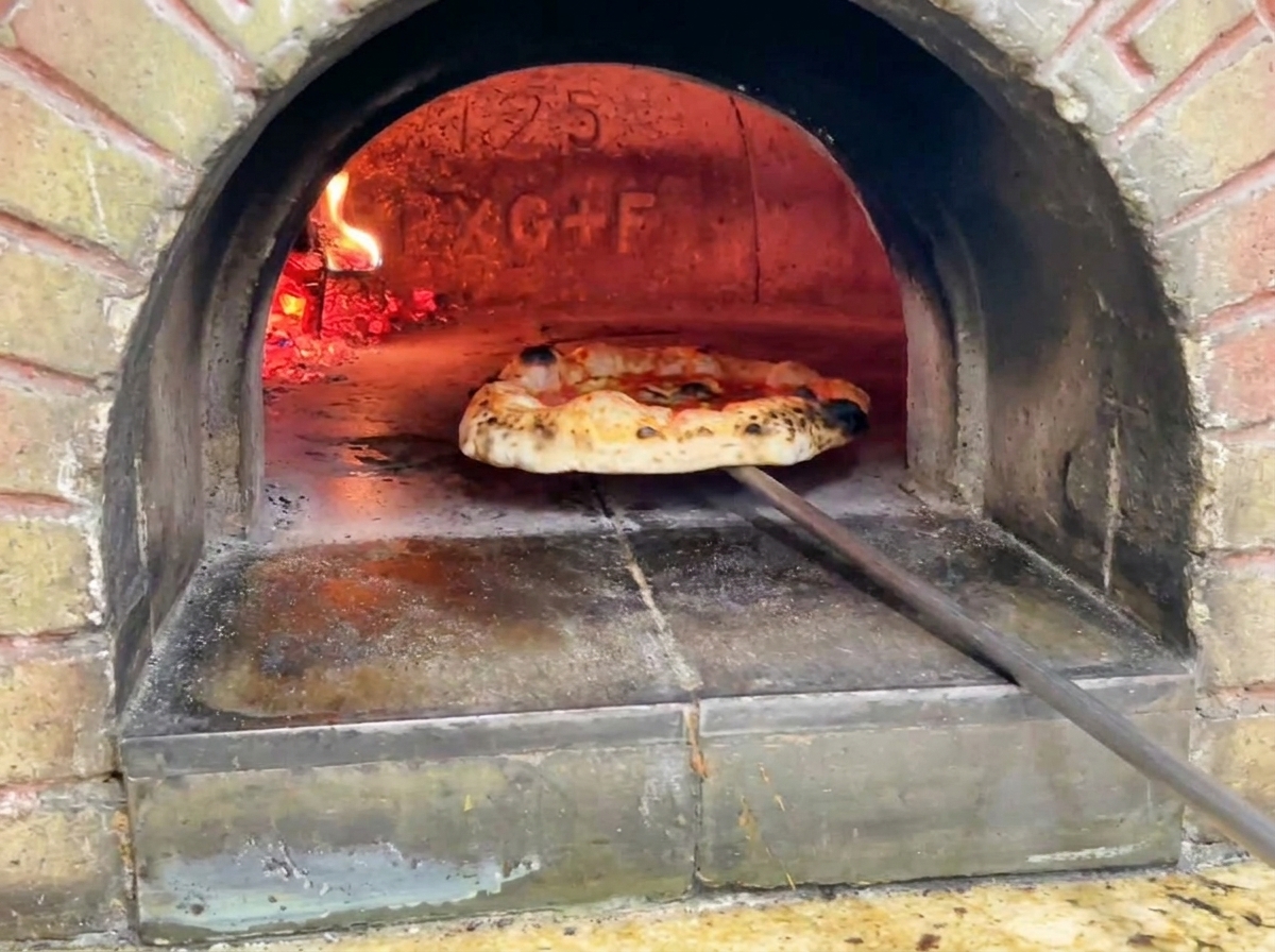 Gotowa pizza wyjmowana z pieca, pokazująca złociste ciasto z ciemnymi przypalonymi plamkami.