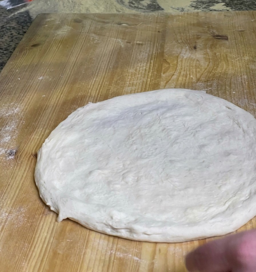 Kucharz rozsmarowujący warstwę intensywnie czerwonego sosu pomidorowego na środku surowego ciasta do pizzy na drewnianej desce.