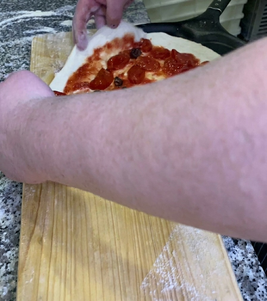 Kucharz zsuwający surową pizzę z dodatkami z drewnianego blatu na czarną metalową łopatę do pizzy.