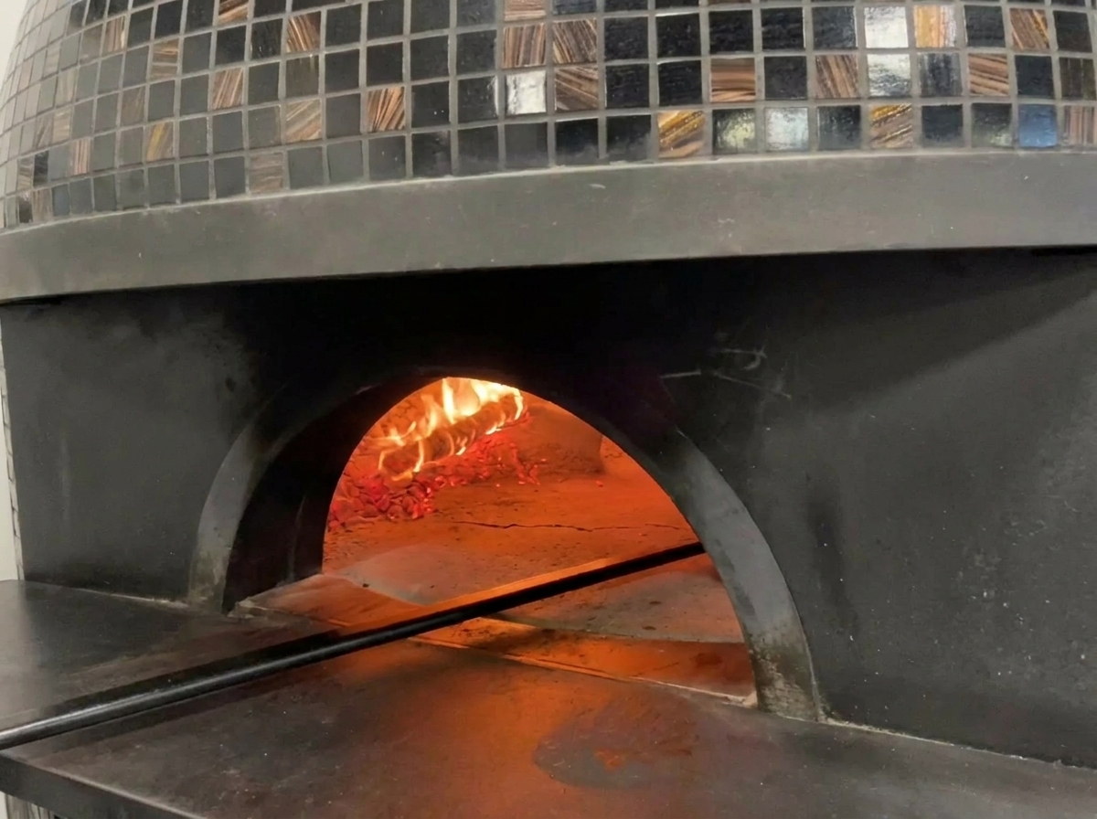 Widok na wnętrze tradycyjnego, opalanego drewnem pieca do pizzy z płomieniami i piekącą się w środku pizzą.