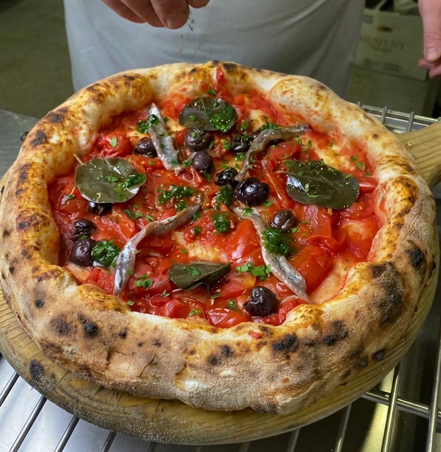 Dłoń posypująca środkową część upieczonej pizzy Marinara świeżą zieloną dekoracją.