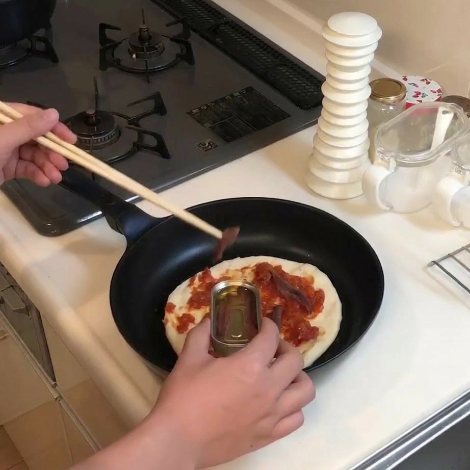 Używanie drewnianych pałeczek do nakładania anchois z puszki na pizzę z sosem.