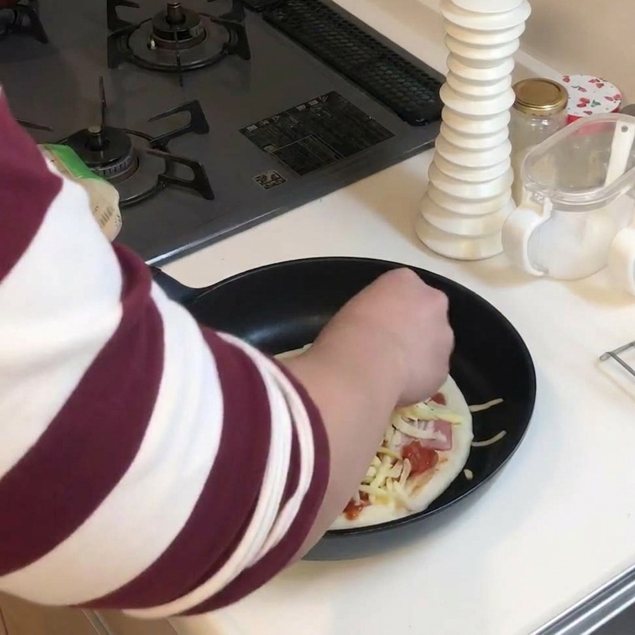 Ręka posypująca grubą warstwę startego żółtego i białego sera na pizzę na patelni.