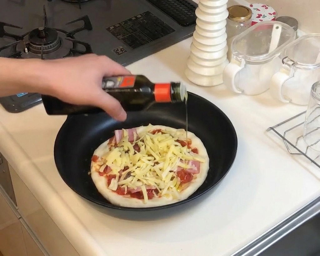 Zbliżenie na dłoń skrapiającą oliwą przygotowaną pizzę na patelni z serem i boczkiem.