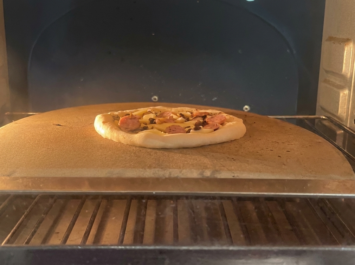 Surowa pizza z pepperoni i grzybami na kamieniu do pieczenia wewnątrz profesjonalnego pieca.