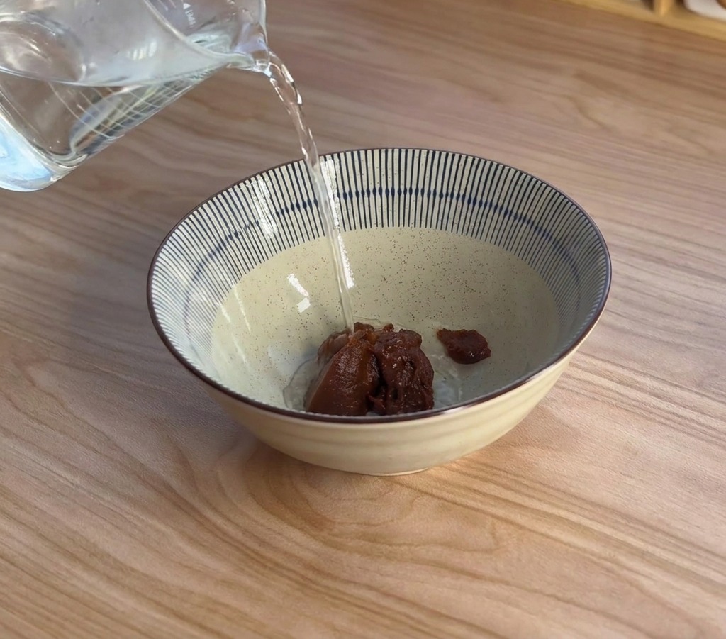 Para unosząca się nad ceramiczną miską podczas wlewania wrzątku do ciemnej pasty miso.