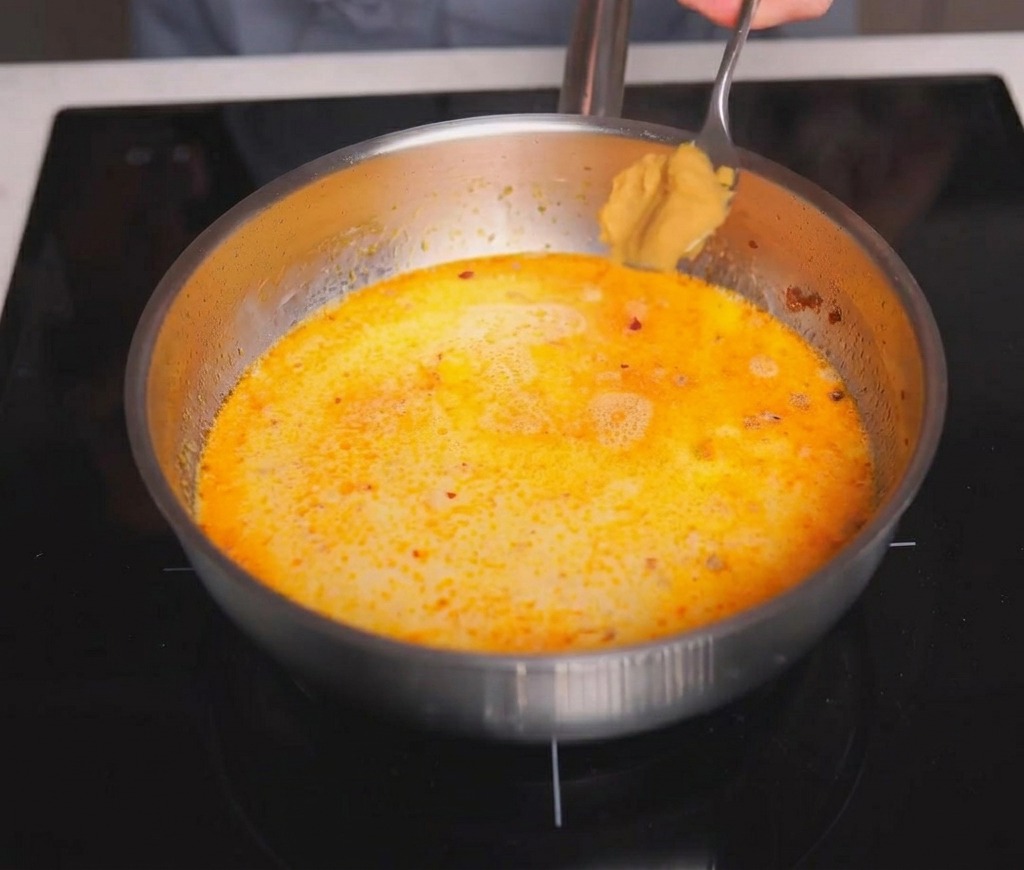Łyżka jasnobrązowej pasty miso dodawana do gotującego się kremowego bulionu.