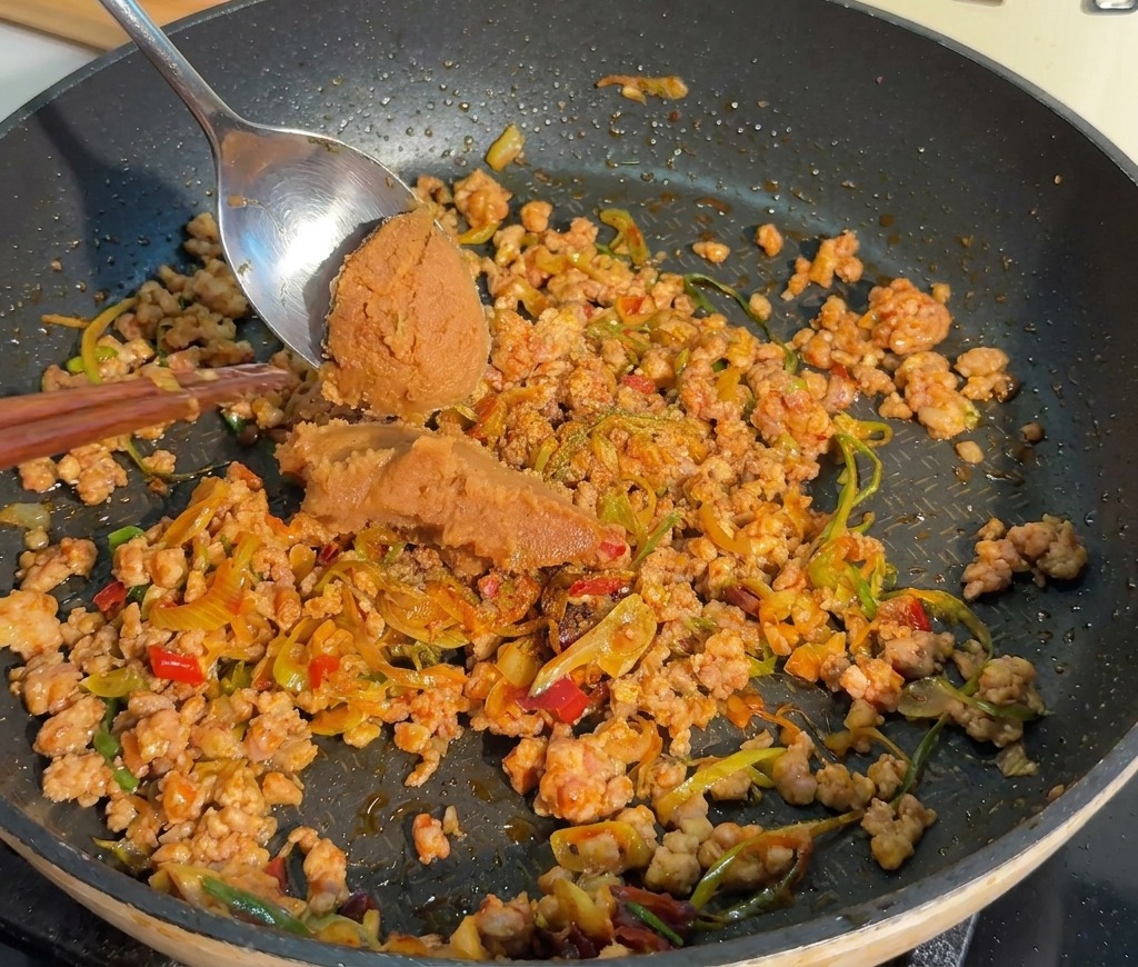 Łyżka nakłada porcję gęstej pasty miso do mięsa na patelni.