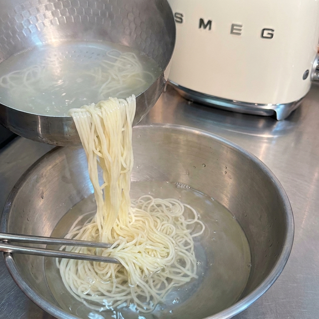 Makaron ramen płukany w misce z zimną wodą za pomocą pałeczek.