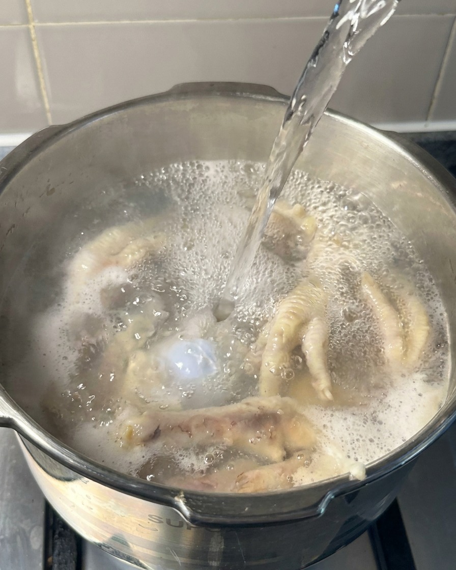 Wrząca woda wlewana do garnka zawierającego częściowo ugotowane kurze łapki i kości wieprzowe.