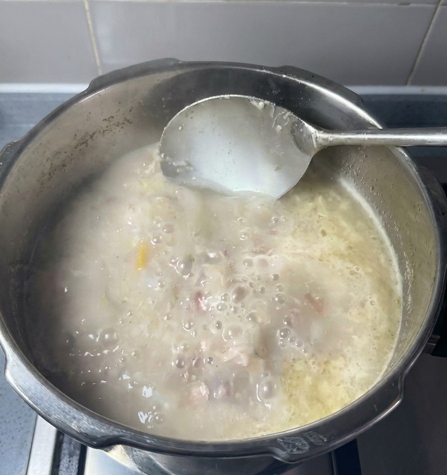 Duża chochla mieszająca w garnku nieprzejrzysty, mlecznobiały wywar z widocznymi kawałkami mięsa i tłuszczu.