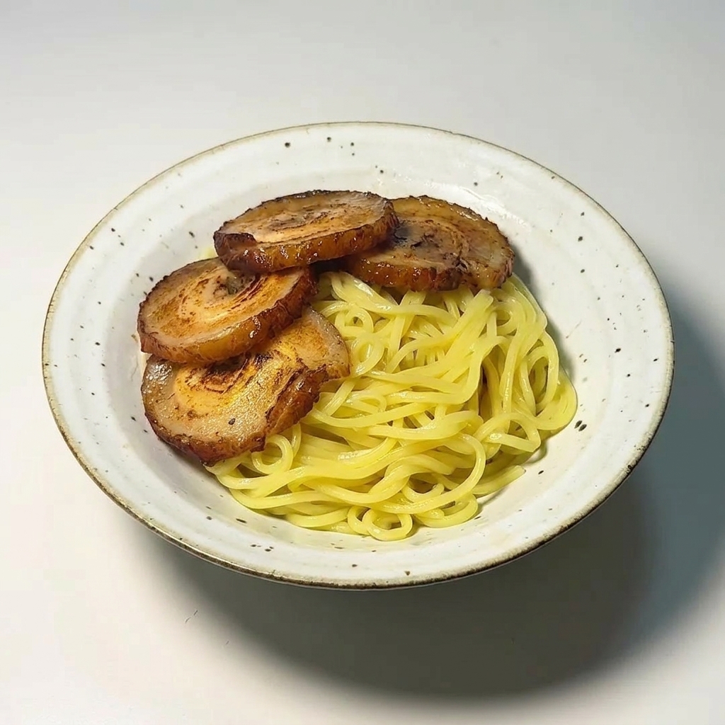Cztery plastry przyrumienionego boczku chashu ułożone schludnie na żółtym makaronie ramen w białej misce.