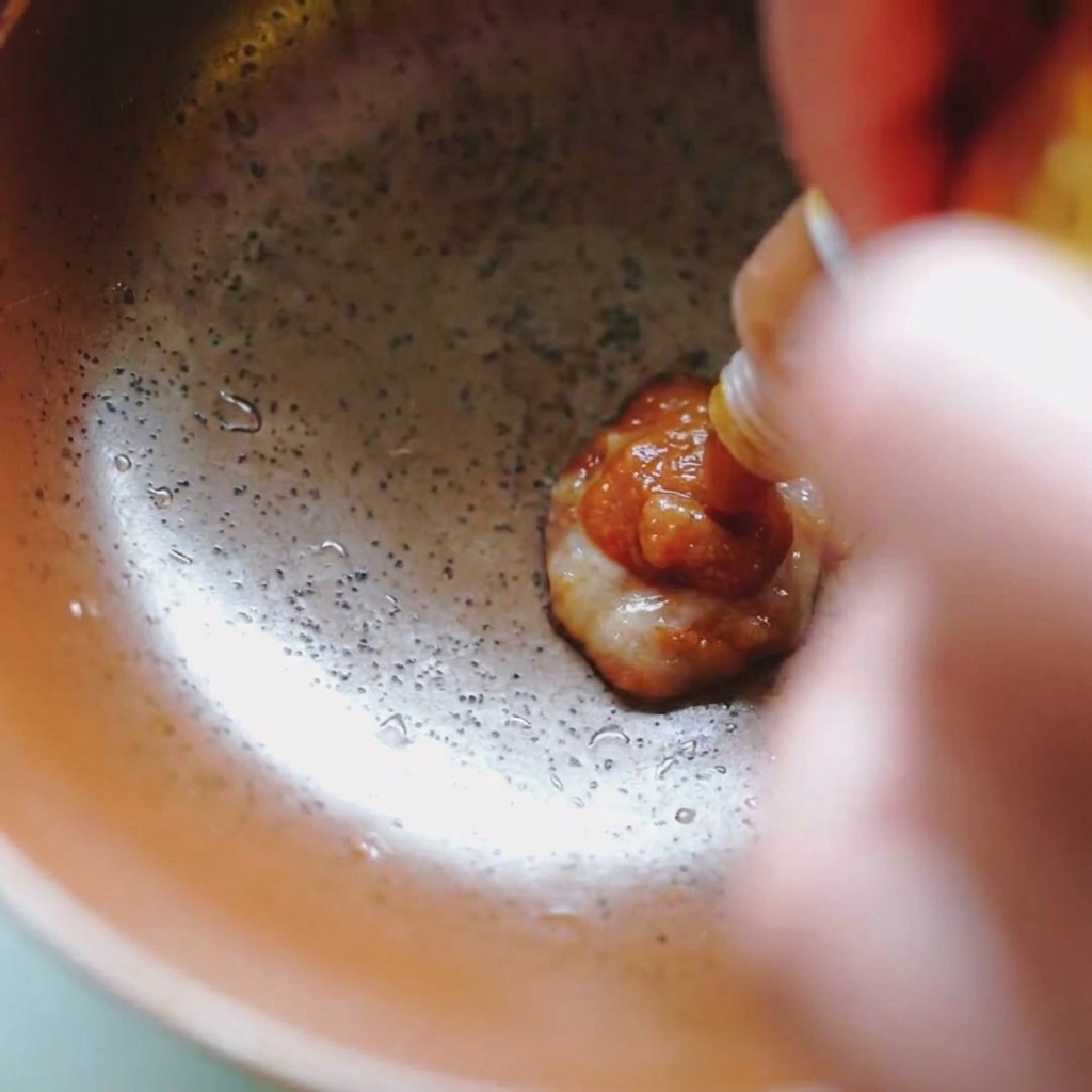Gęsta, brązowa pasta miso wyciskana z małej saszetki do brązowej ceramicznej miski.