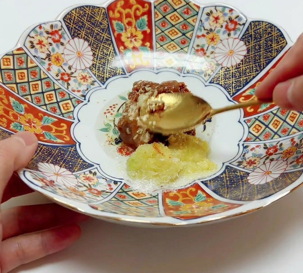 Złota łyżka mieszająca i łącząca pastę miso z aromatami i olejem w dużej wzorzystej misce ceramicznej.