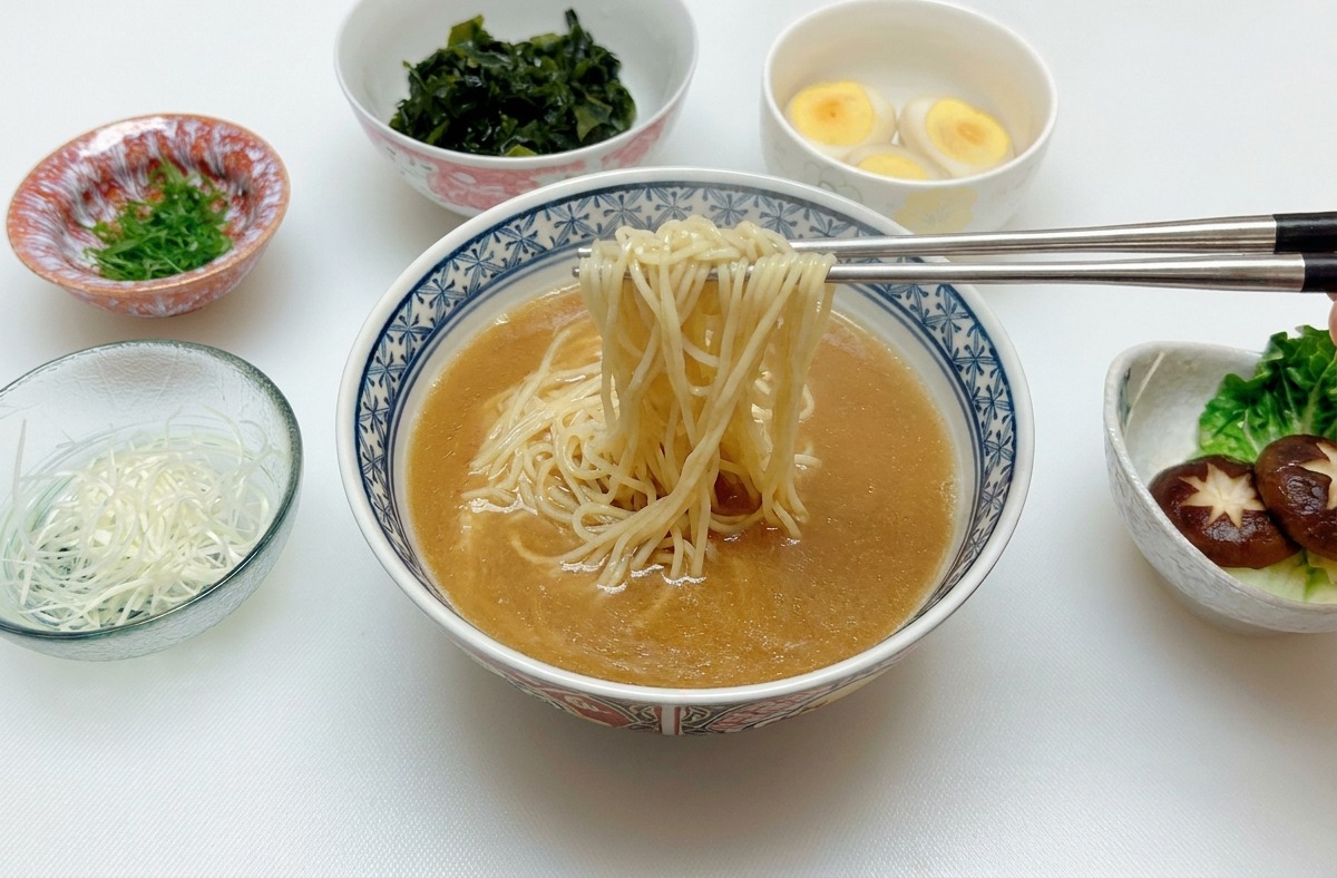 Para srebrnych pałeczek podnosząca i centrująca makaron ramen w misce z brązowym wywarem miso.