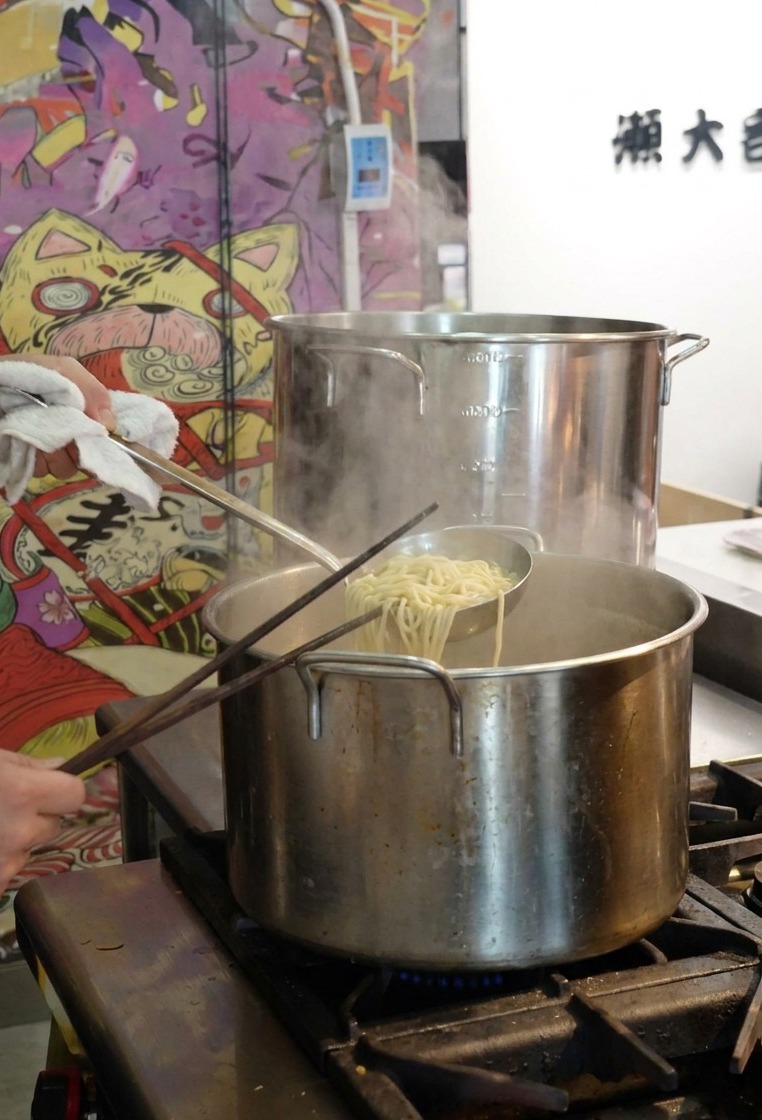 Podnoszenie sitka z makaronem ramen nad garnkiem z wrzącą wodą.
