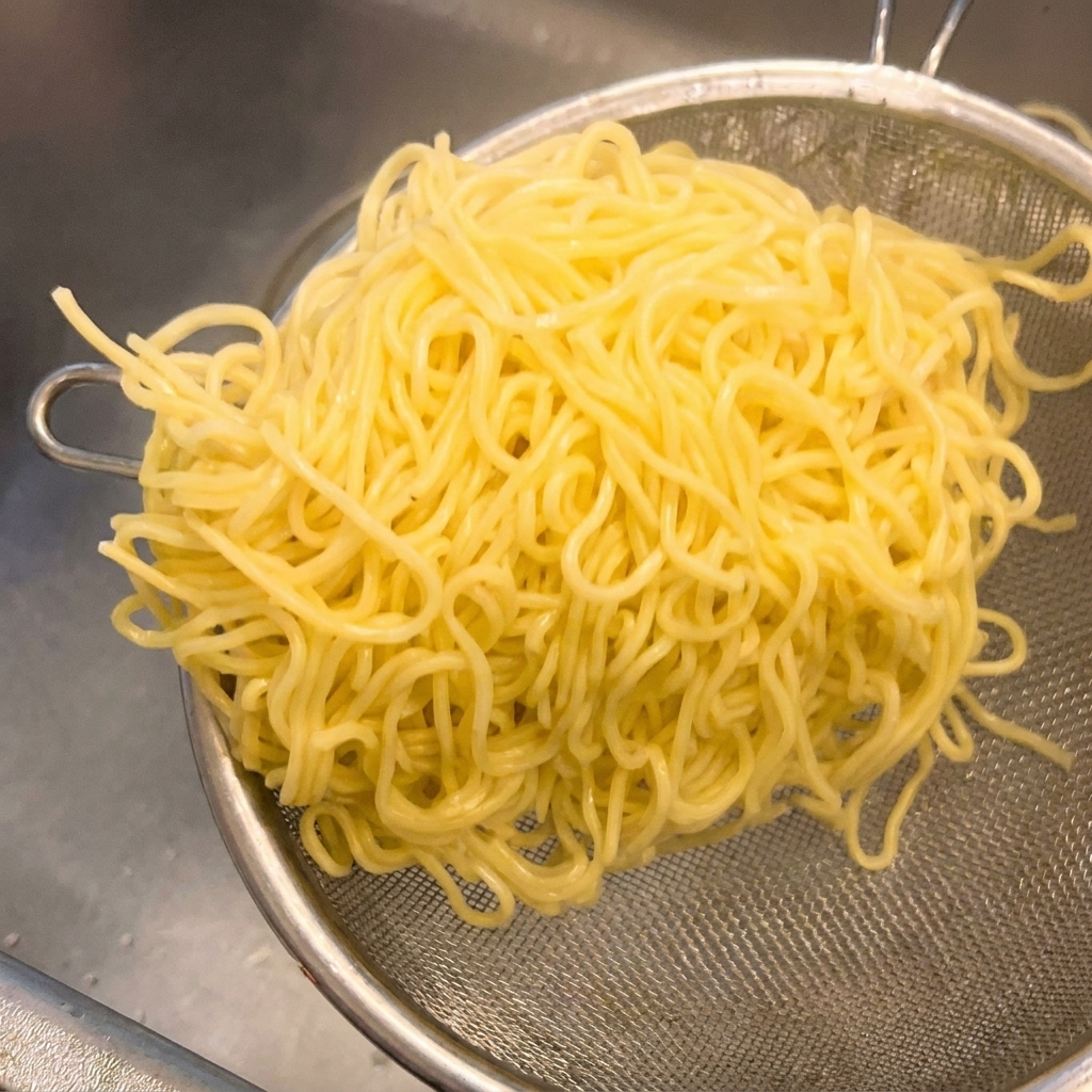 Ugotowany żółty makaron ramen na metalowym sitku, energicznie potrząsany w celu usunięcia wody.