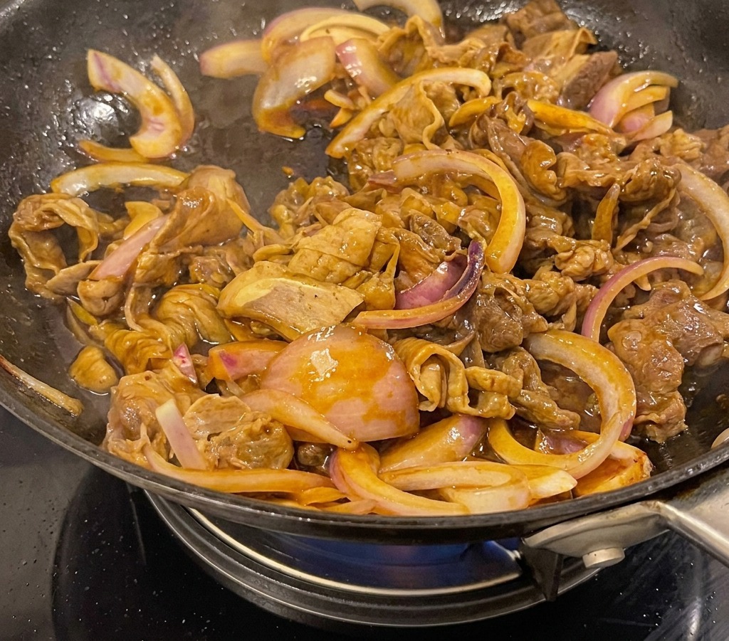Wołowina teriyaki z cebulą dusząca się w gęstym, ciemnym, lśniącym sosie w czarnym woku.