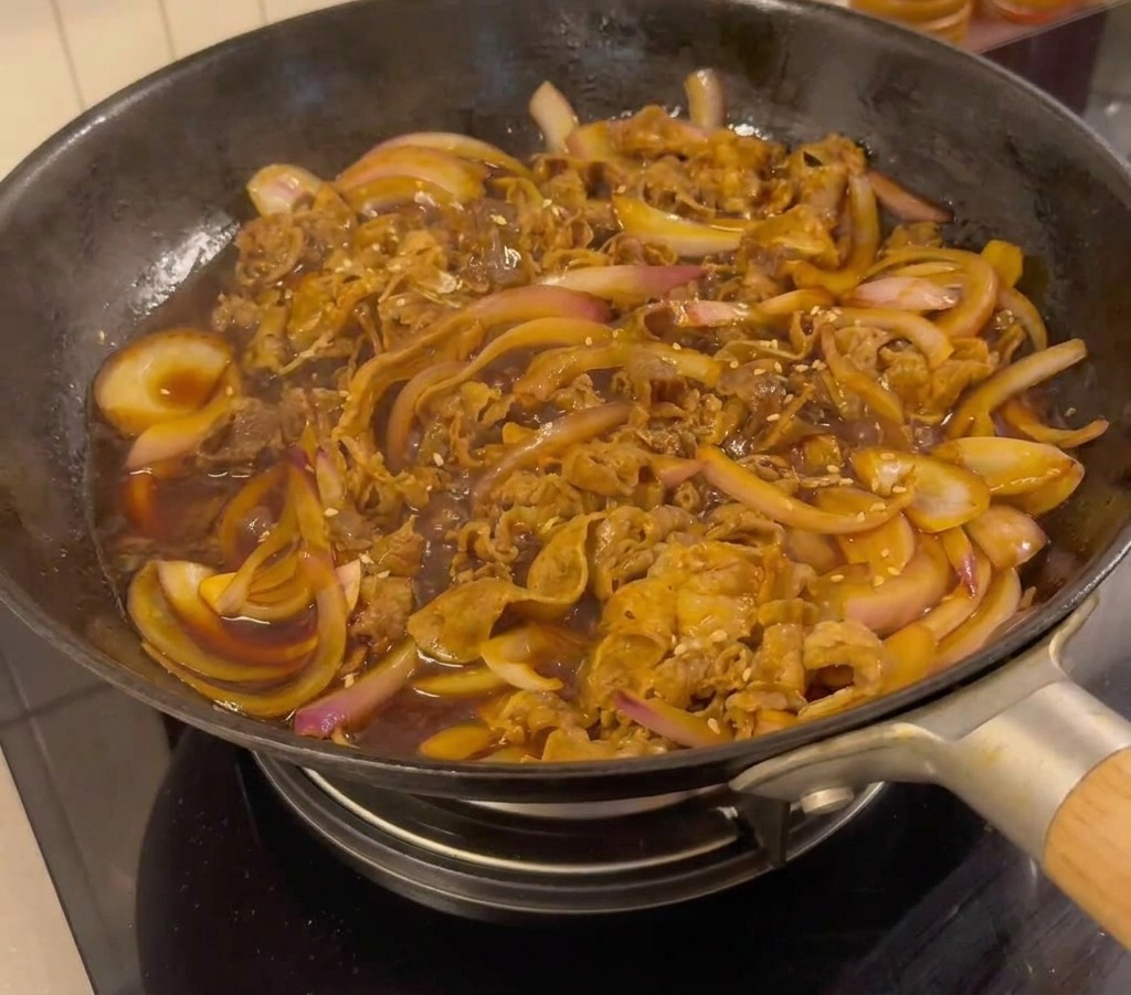 Gotowa wołowina teriyaki na patelni, posypana białym sezamem i dymką.