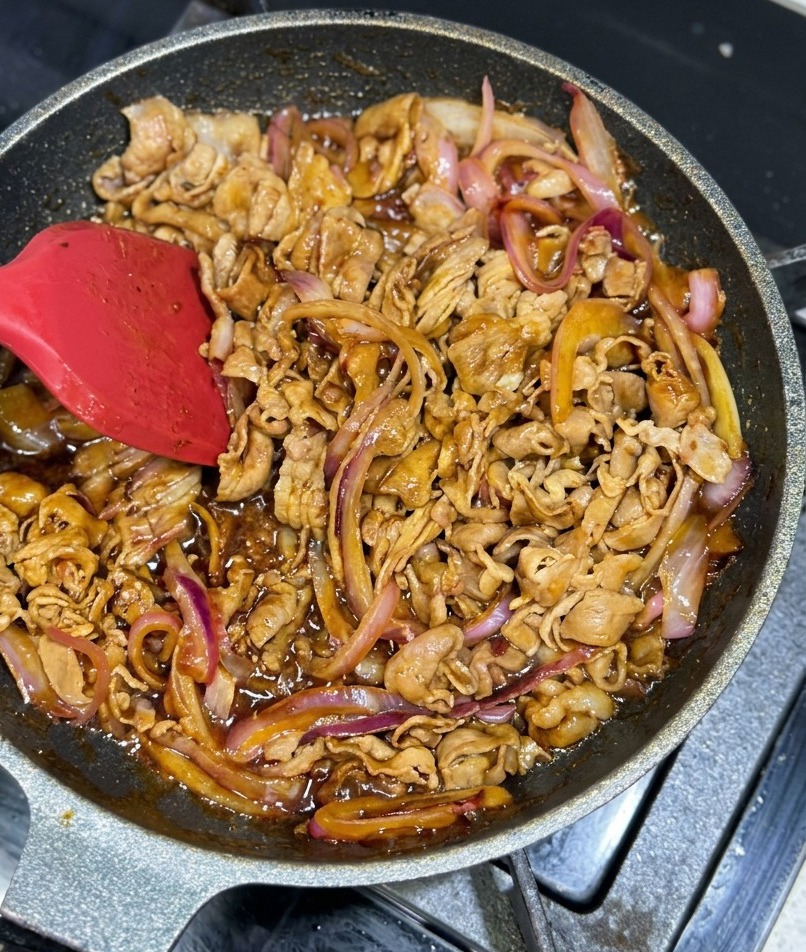 Cienkie plastry wołowiny i cebuli mieszane na patelni w gęstej, lśniącej brązowej glazurze.