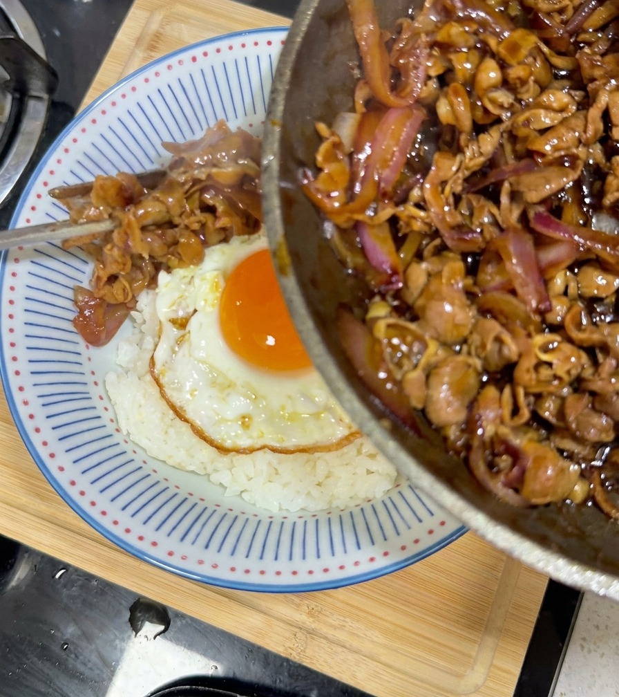 Wołowina teriyaki z cebulą nakładana z patelni do miski z ryżem i jajkiem.