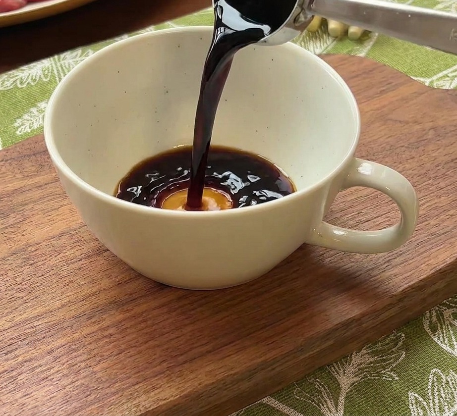 Metalowa łyżka wlewająca ciemny sos sojowy do ceramicznej miski z wodą i porcją czerwonej pasty chili.