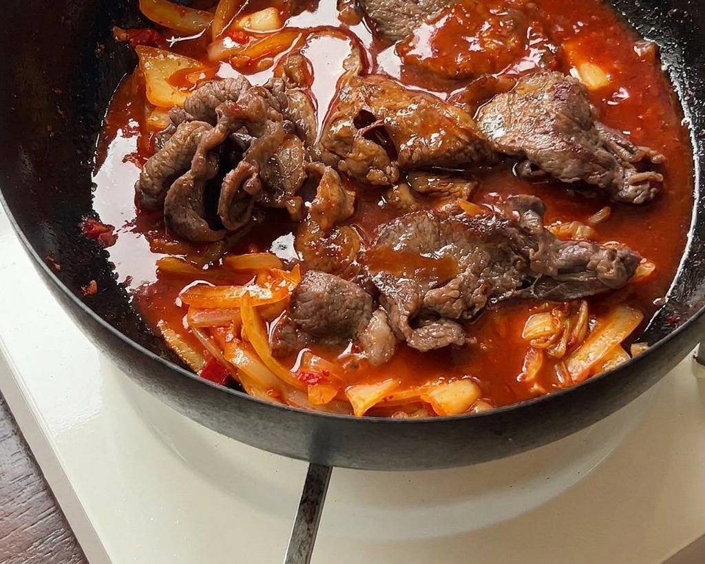 Wołowina z kimchi dusząca się w gęstym, czerwonym sosie na czarnej żeliwnej patelni.