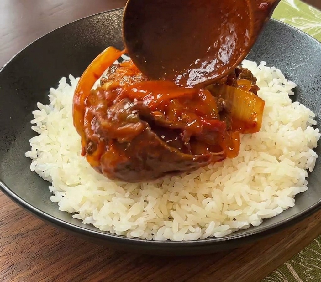 Drewniana łyżka nakładająca porcję wołowiny z kimchi w sosie na biały ryż w czarnej misce.