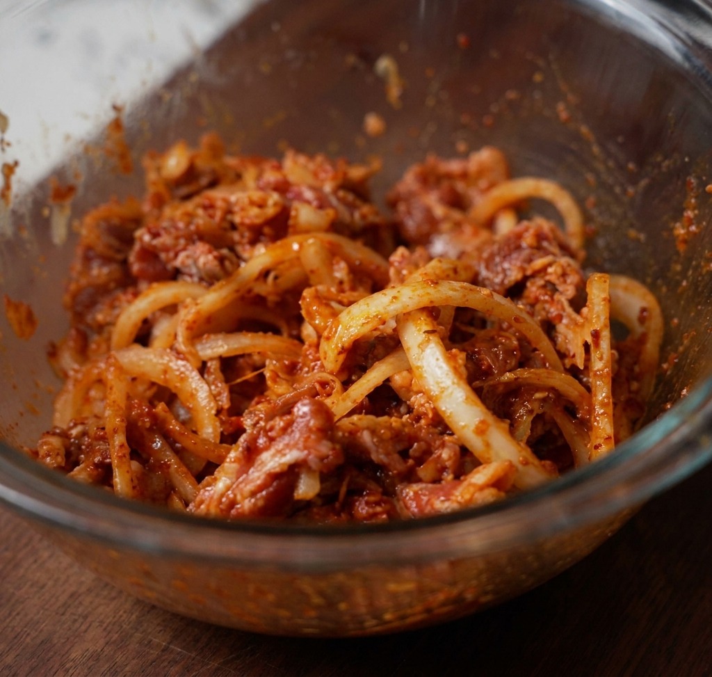 Cienko pokrojona wołowina, biała cebula i czerwona pasta chili dokładnie wymieszane w przezroczystej szklanej misce.