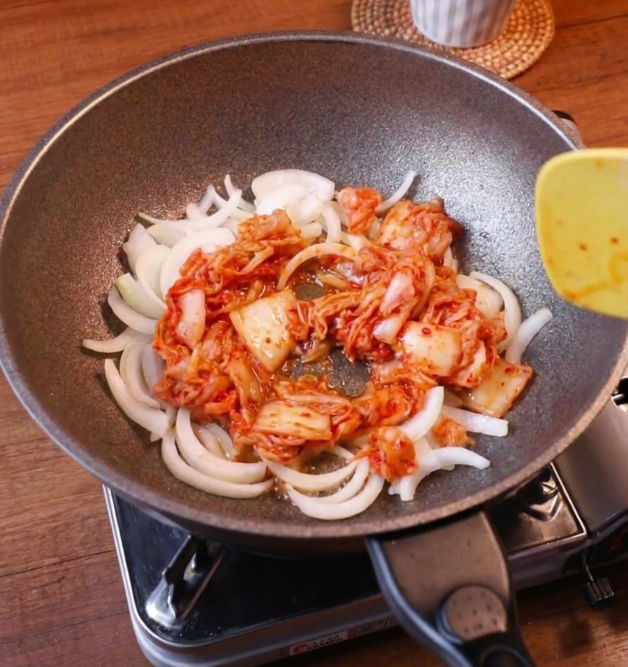 Smażenie białej cebuli i czerwonego kimchi na patelni przy użyciu łopatki.