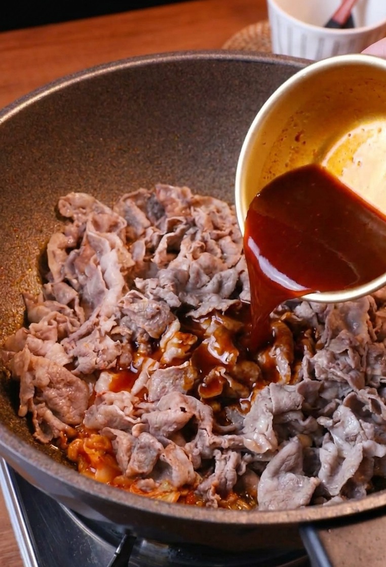 Polewanie smażonej wołowiny i kimchi ciemnym, aromatycznym sosem z miseczki.