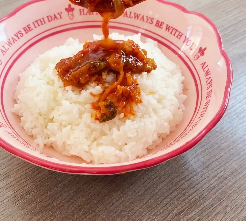 Aromatyczna mieszanka kimchi i wołowiny nakładana łyżką na porcję białego ryżu w różowej misce.