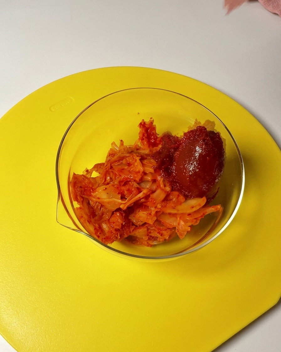 Łyżka czerwonej pasty gochujang i płatków chili dodawana do szklanej miski z posiekanym kimchi.