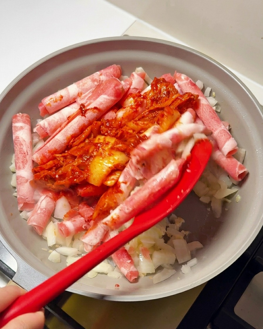 Czerwona łopatka nakładająca sos z kimchi i pasty chili na wołowinę i cebulę na patelni.