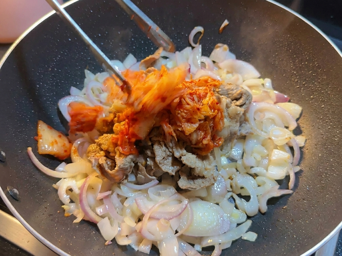 Posiekane kimchi z kapusty nakładane szczypcami do woka z wołowiną i cebulą.