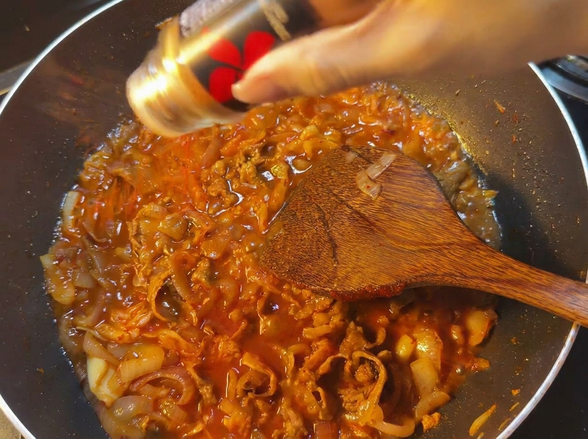 Czerwona papryka chili sypana z czarnego pojemnika do patelni z gotującym się czerwonym sosem.